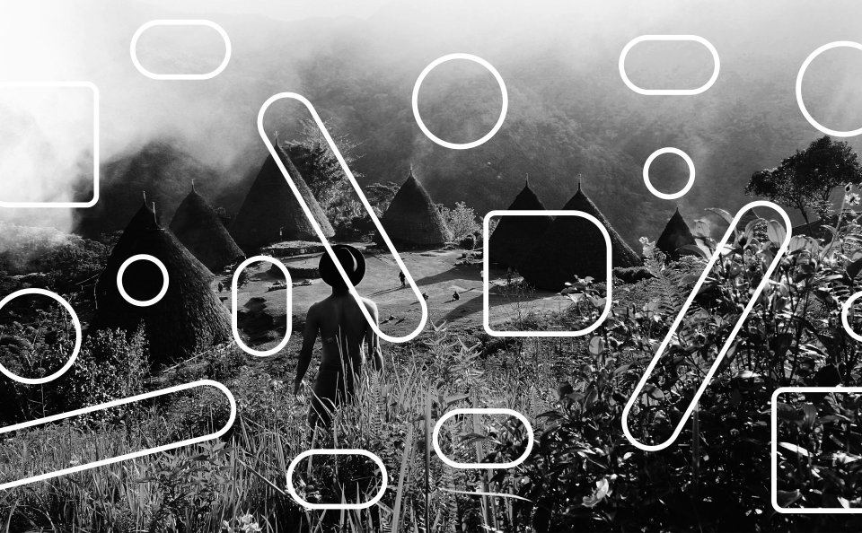 A man in a hat stands with his back to us, looking at the Indonesian village of Wae Rebo with its conical huts. black and white photograph overlaid with a white Nuraga Budaya raster